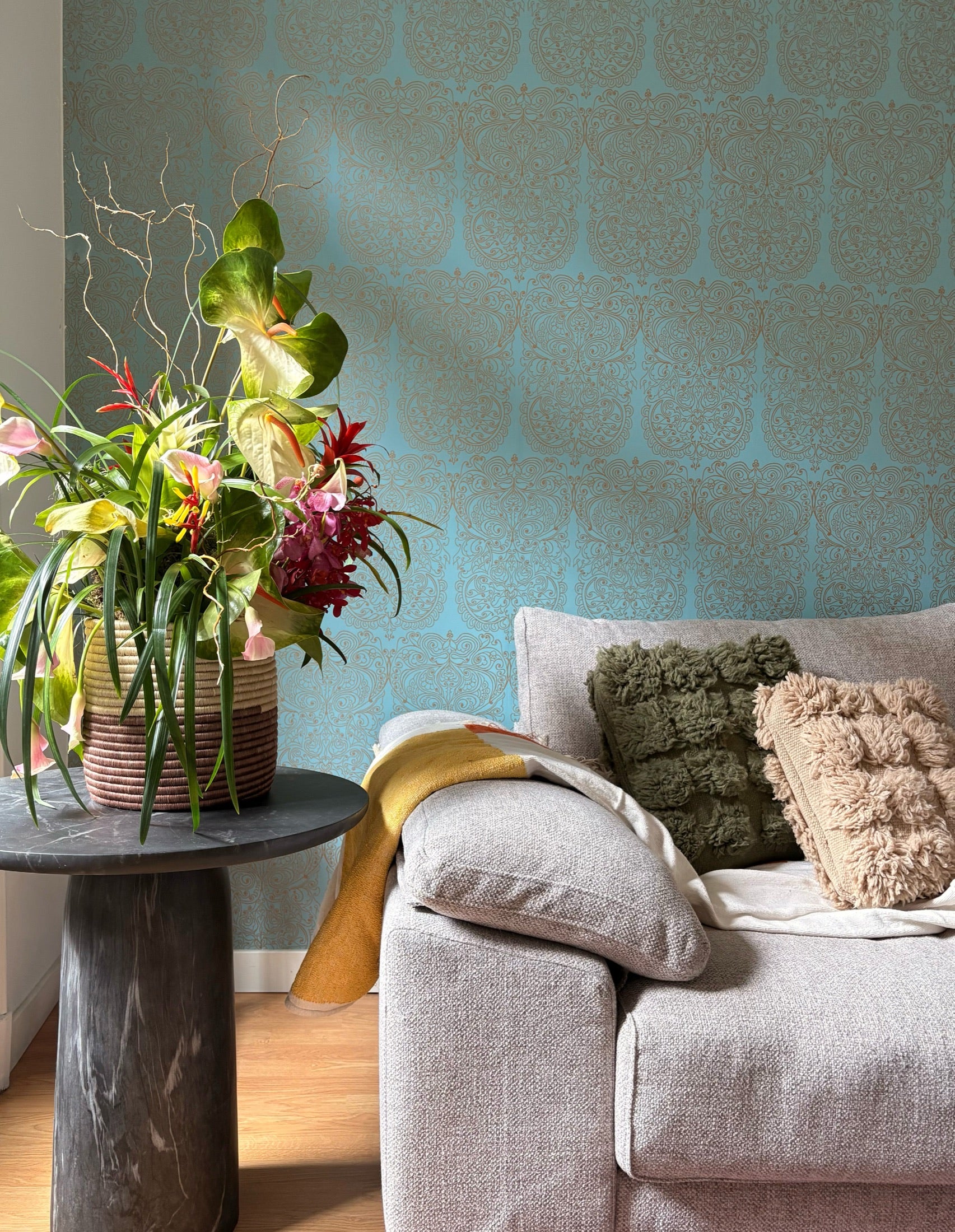 A basket of flowers on a marble side table beside a sofa with handmade tufted pillows